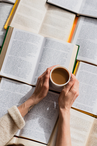 cropped view of woman holding cup of coffee near open books