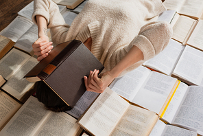 tattooed woman obscuring face while lying on pile of open books