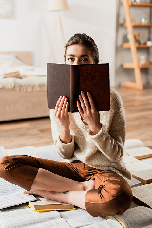 woman obscuring face while sitting on pile of books