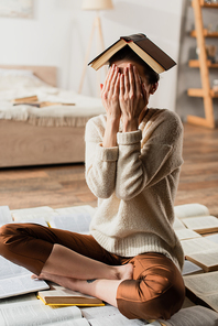 young woman obscuring face while sitting on pile of books