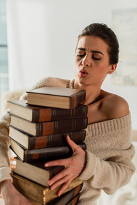 young woman looking at pile of books at home