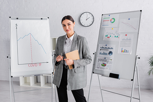 Young businesswoman in earphone with pen and notebook  near flipchart with graphs