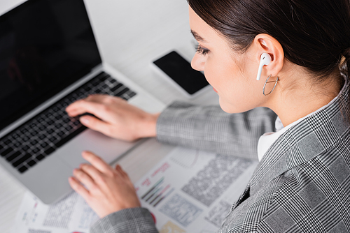 Businesswoman in earphone using laptop on blurred background