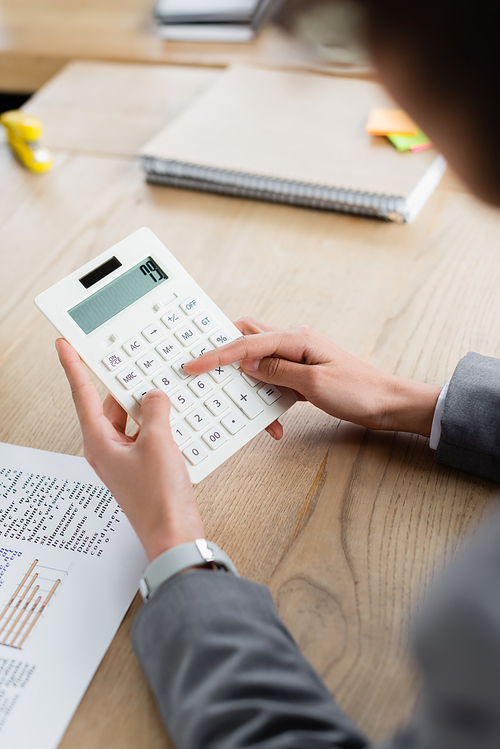 Cropped view of businesswoman using calculator near document and blurred notebook