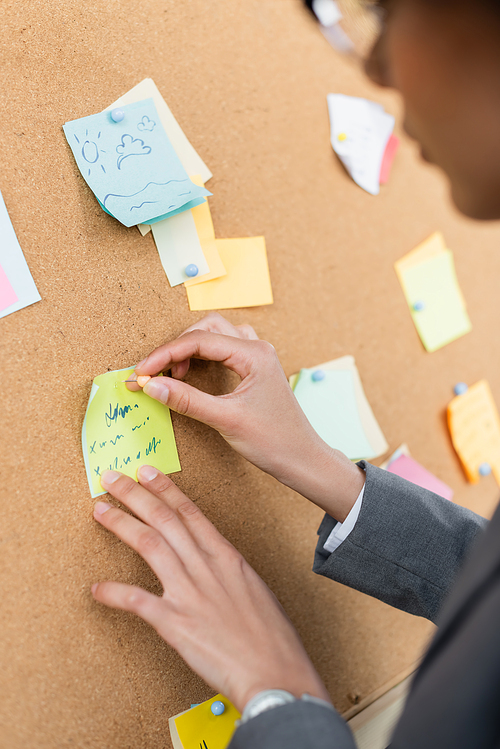 Cropped view of african american businesswoman attaching sticky note on wooden board