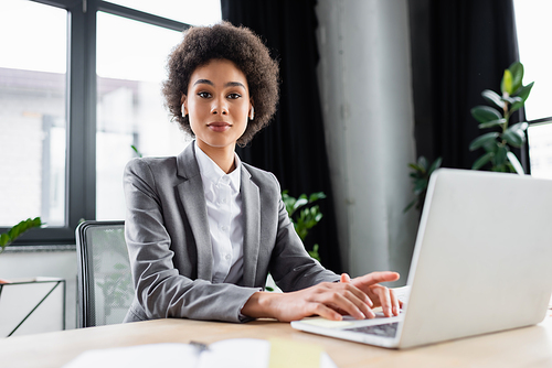 African american businesswoman in earphones  near blurred laptop