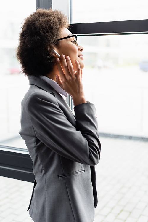 Side view of african american businesswoman in earphone standing near window