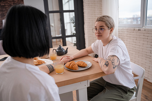 tattooed lesbian couple holding hands and looking at each other in kitchen