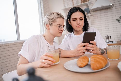 brunette woman using smartphone near girlfriend in kitchen