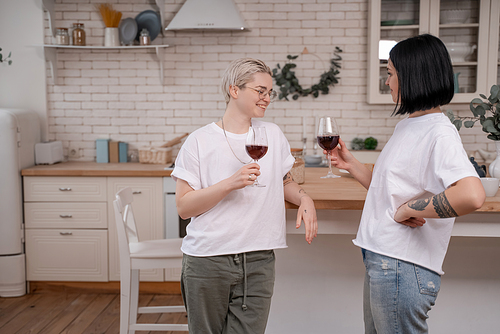 happy lesbian couple holding glasses of red wine in kitchen