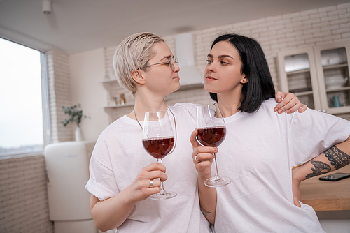 woman in glasses hugging girlfriend while holding glasses of red wine