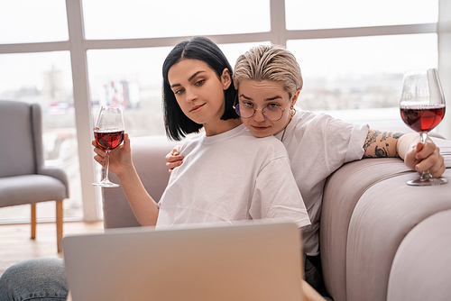 lesbian couple watching movie on laptop while holding glasses of red wine