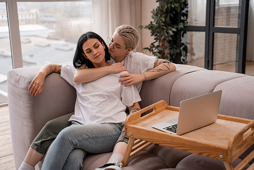 lesbian couple watching movie on laptop while chilling on sofa