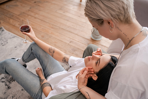 blurred tattooed woman looking at girlfriend with glass of red wine