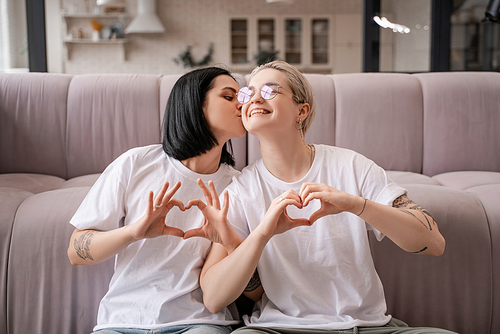 happy lesbian couple showing heart sign with hands in living room