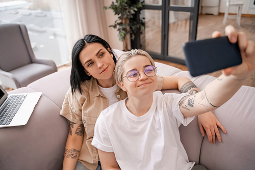 woman smiling with happy girlfriend in glasses taking selfie in living room