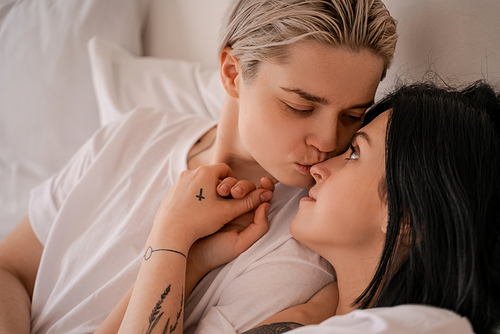 young woman lying in bed and kissing nose of girlfriend