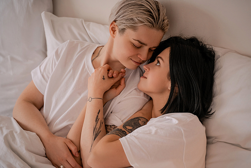 loving young lesbian couple lying in bed and holding hands