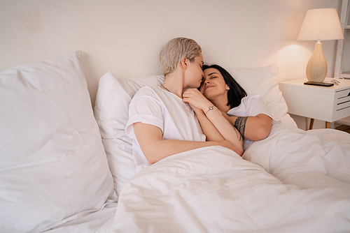 young lesbian couple lying in bed, smiling and holding hands