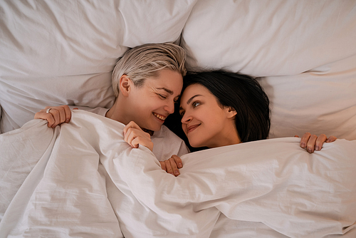 top view of happy lesbian couple lying in bed under blanket