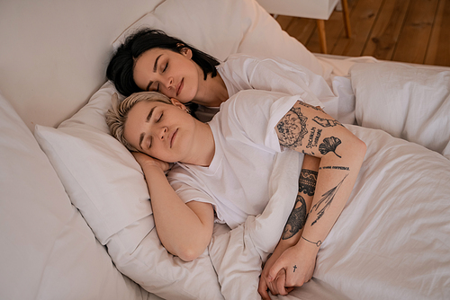 high angle view of young lesbian couple lying in bed and holding hands