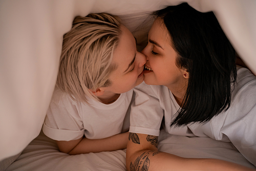 young lesbian couple kissing under blanket