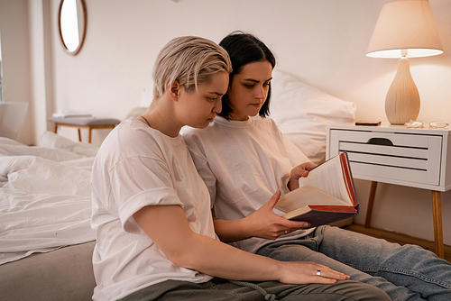 young lesbian couple reading book in bedroom