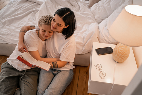 high angle view of happy young lesbian couple reading book in bedroom