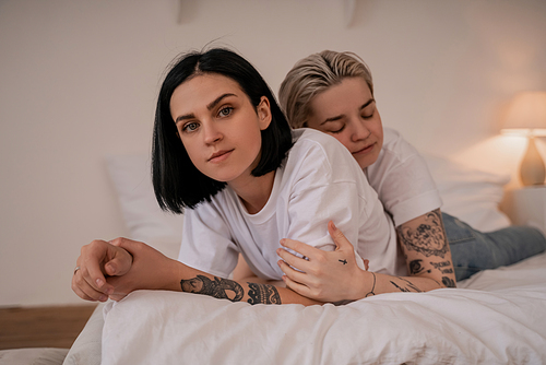 young lesbian woman hugging tattooed girlfriend and lying on bed