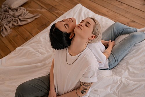 high angle view of lesbian couple sitting back to back on bed