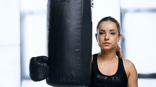 young sportswoman in boxing glove resting near punching bag in gym