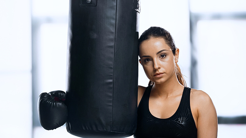 tired sportswoman in boxing glove resting near punching bag