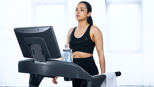 sporty woman in sportswear exercising on treadmill near sports bottle with water in gym