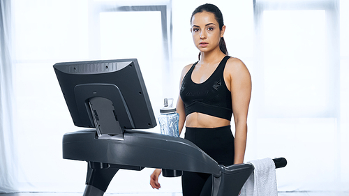 sporty woman in sportswear on treadmill near sports bottle with water in gym