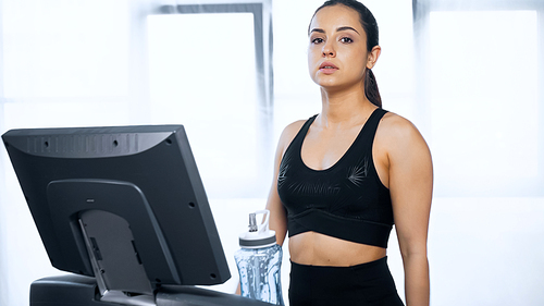 young woman in sportswear exercising on treadmill near sports bottle with water in gym