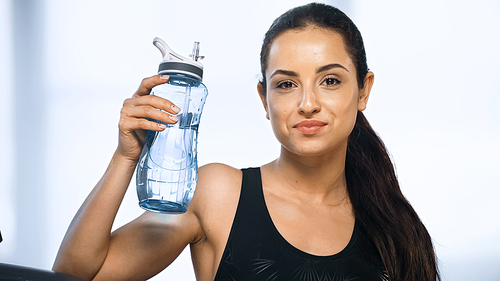 young sportive woman holding sports bottle with water in gym