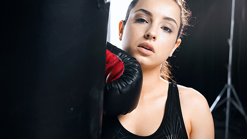 tired sportswoman in boxing glove leaning on punching bag in gym