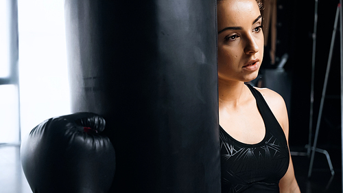 tired sportswoman in boxing glove leaning on punching bag