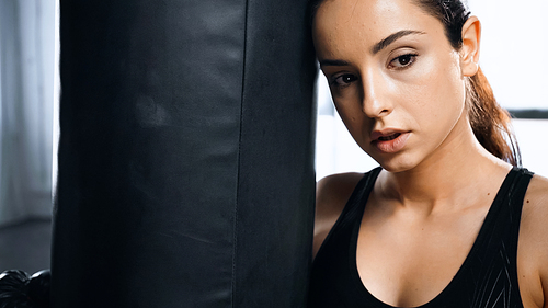 tired young sportswoman leaning on punching bag in gym