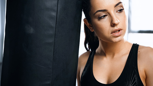 exhausted sportswoman leaning on punching bag in gym