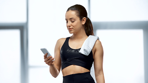 young sportswoman with towel looking at smartphone in gym