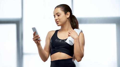 young sportswoman with towel using smartphone in gym
