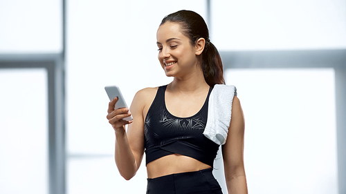happy sportswoman with towel using smartphone in gym