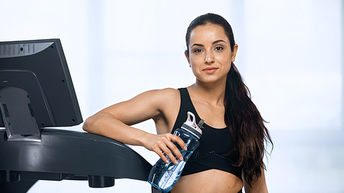 sporty woman in sportswear holding sports bottle with water near treadmill