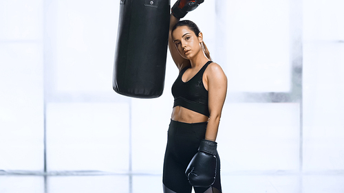 exhausted sportswoman in boxing gloves leaning on punching bag in gym