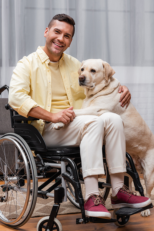 disabled man smiling at camera while cuddling labrador at home