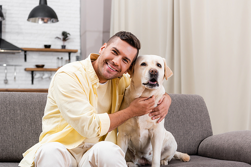 happy man smiling at camera while embracing labrador dog