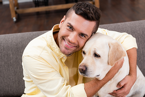 young man embracing labrador dog while smiling at camera