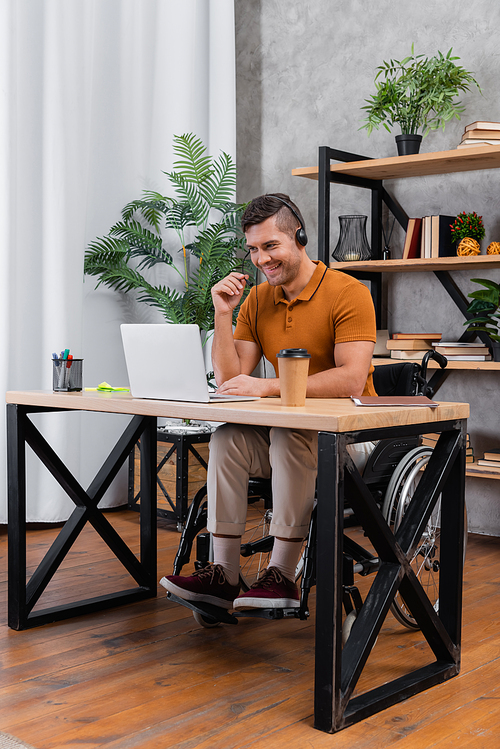 cheerful, disabled man in headset working in home office near laptop