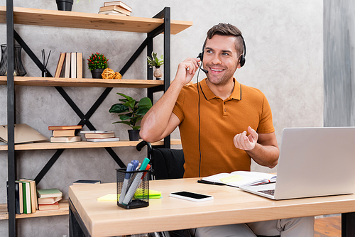 joyful man in headset working at home neat laptop and smartphone with blank screen